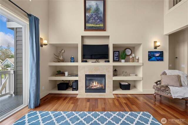 living area with a fireplace, built in features, wood finished floors, and a towering ceiling