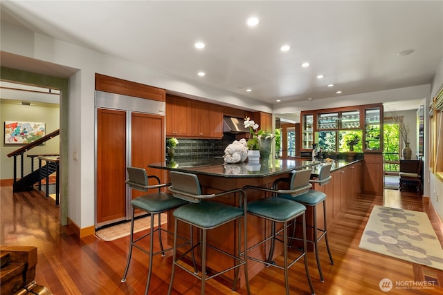 kitchen with wall chimney range hood, a breakfast bar area, dark hardwood / wood-style floors, and paneled built in fridge