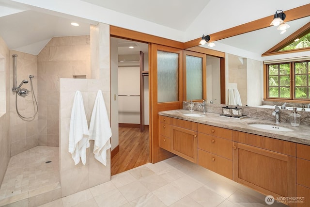 bathroom with lofted ceiling, vanity, and a tile shower