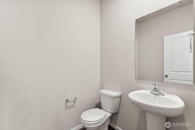 half bathroom featuring toilet, baseboards, and a sink