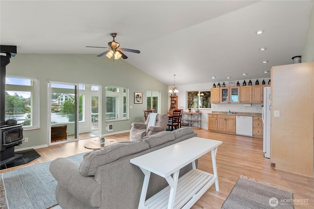 living room with lofted ceiling, light wood-style flooring, a wood stove, baseboards, and ceiling fan with notable chandelier