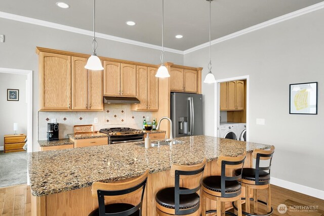 kitchen featuring washing machine and clothes dryer, tasteful backsplash, appliances with stainless steel finishes, a sink, and under cabinet range hood