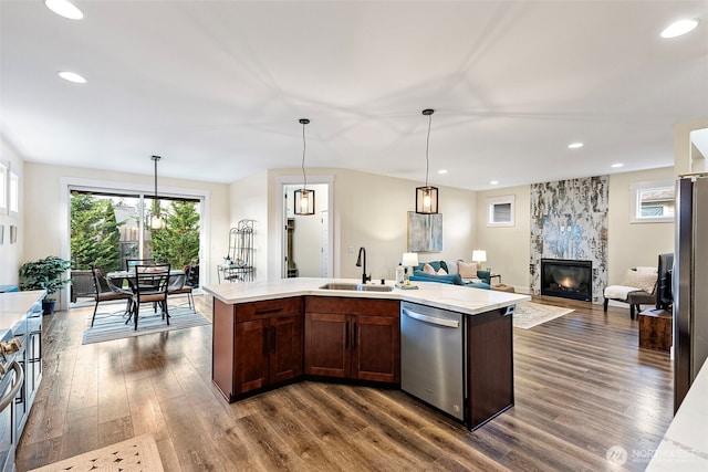 kitchen featuring a tiled fireplace, appliances with stainless steel finishes, open floor plan, dark wood-style flooring, and a sink