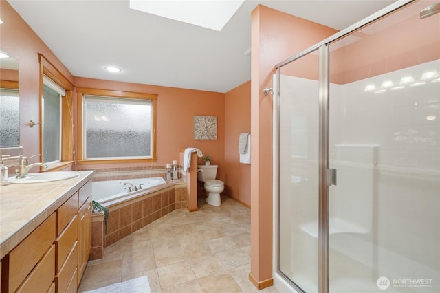 full bathroom featuring a skylight, toilet, a stall shower, vanity, and a bath