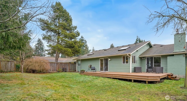 rear view of property featuring a chimney, fence, a deck, and a yard