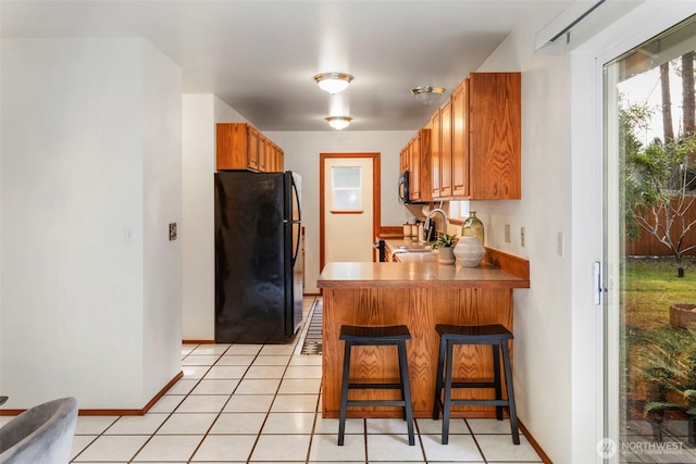 kitchen with a kitchen bar, kitchen peninsula, light tile patterned floors, and black appliances