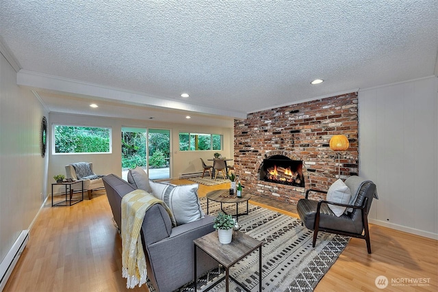 living area with a textured ceiling, baseboard heating, a brick fireplace, light wood finished floors, and crown molding