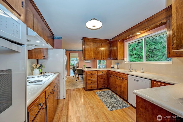 kitchen featuring white appliances, tile countertops, brown cabinets, a peninsula, and under cabinet range hood