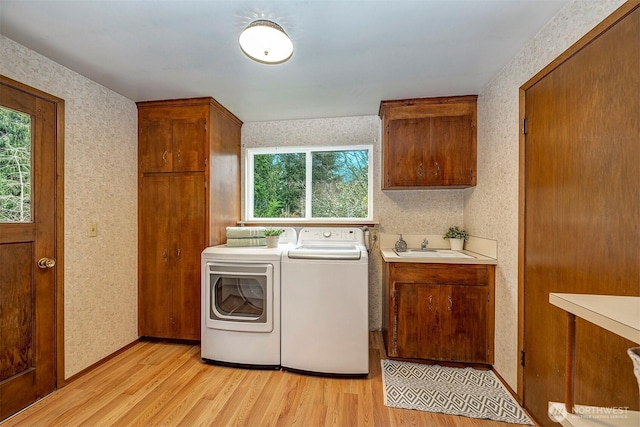 washroom with wallpapered walls, cabinet space, light wood-style flooring, washing machine and dryer, and a sink