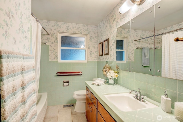 full bath with tile walls, toilet, wainscoting, tile patterned flooring, and wallpapered walls