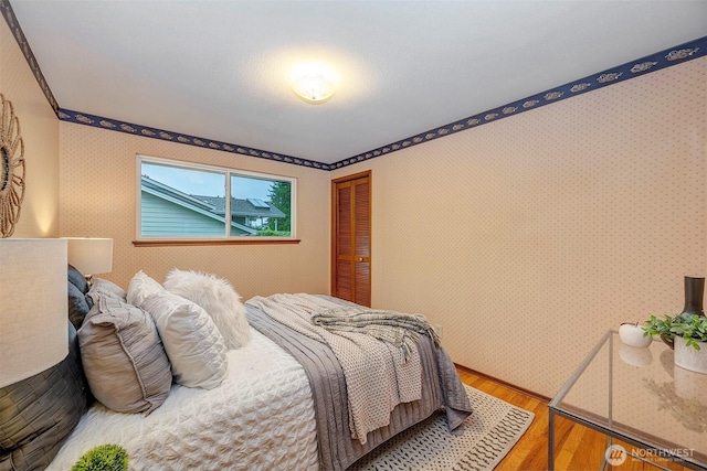 bedroom with a closet, wood finished floors, and wallpapered walls