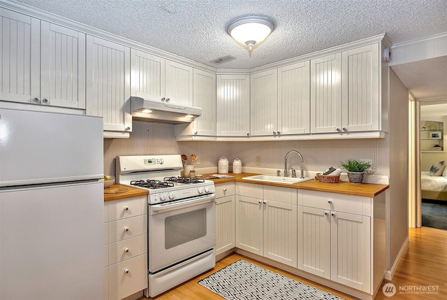 kitchen featuring under cabinet range hood, white appliances, a sink, white cabinets, and wooden counters