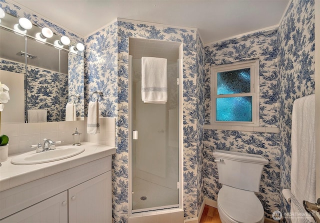 bathroom with a stall shower, vanity, toilet, and wallpapered walls