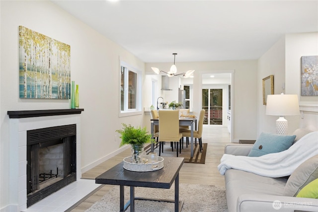 living room featuring light wood-type flooring, a healthy amount of sunlight, a fireplace with flush hearth, and baseboards