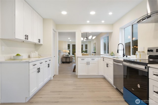 kitchen featuring appliances with stainless steel finishes, white cabinets, a sink, and wall chimney range hood