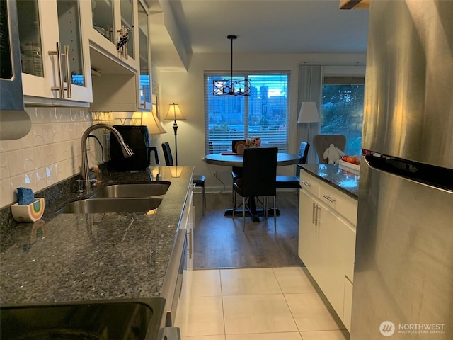 kitchen with hanging light fixtures, stainless steel fridge, sink, backsplash, and white cabinets