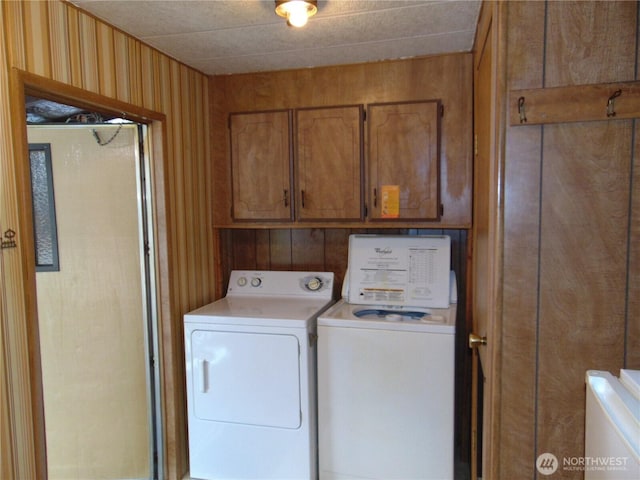 clothes washing area with cabinets, washer and clothes dryer, and wooden walls