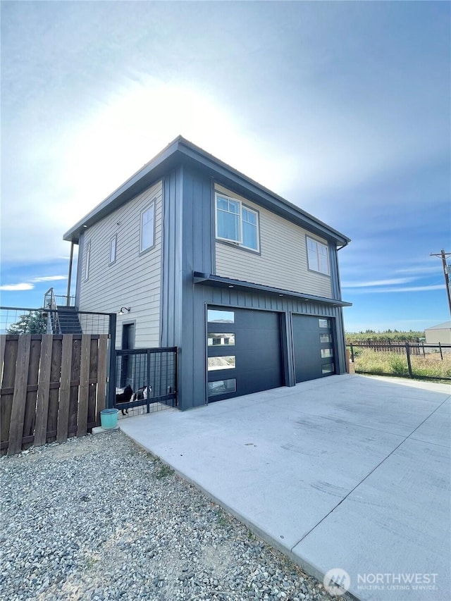 view of side of property featuring a garage, driveway, board and batten siding, and fence