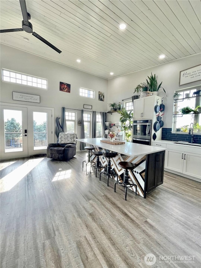 kitchen with light wood-style flooring, wooden ceiling, a sink, and stainless steel oven