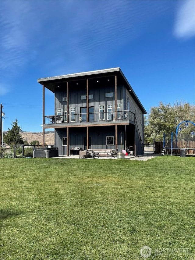 back of house with a trampoline, fence, a lawn, board and batten siding, and a patio area