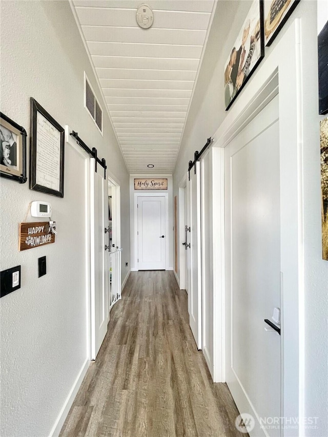 hall featuring wood finished floors, visible vents, baseboards, and a barn door