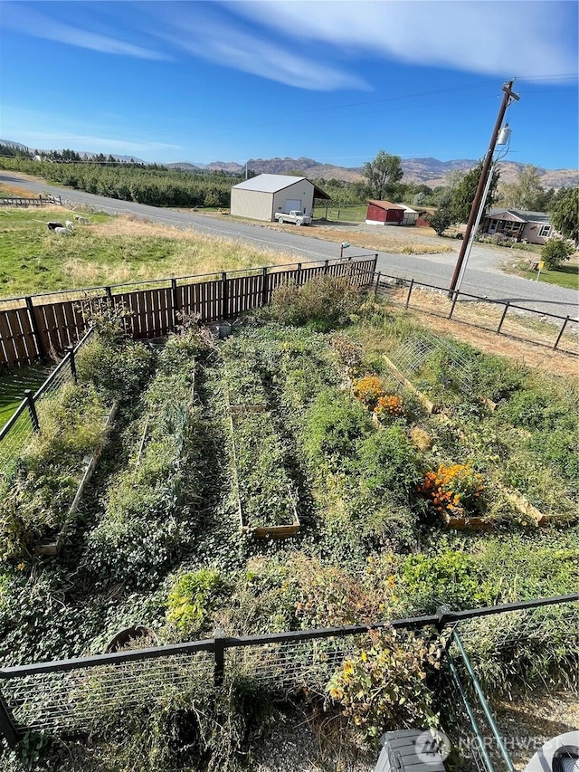 view of yard with a rural view, an outdoor structure, fence, a vegetable garden, and a pole building