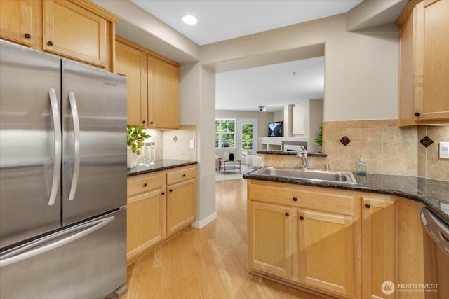 kitchen featuring light wood finished floors, dark stone countertops, stainless steel appliances, light brown cabinetry, and a sink