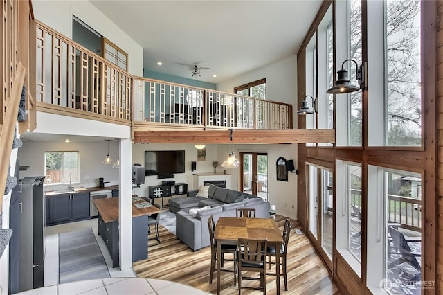 living room with a fireplace, a ceiling fan, light wood finished floors, and a towering ceiling