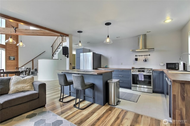 kitchen with wall chimney range hood, appliances with stainless steel finishes, a healthy amount of sunlight, and open floor plan