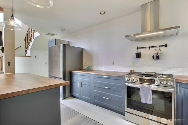 kitchen with wood counters, wall chimney exhaust hood, stainless steel appliances, decorative light fixtures, and visible vents