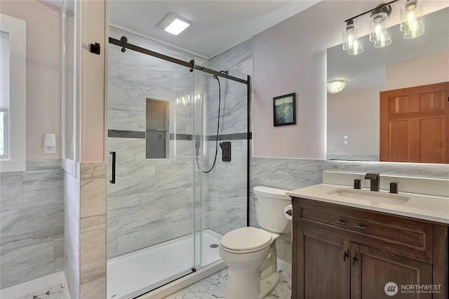 bathroom featuring vanity, toilet, marble finish floor, tile walls, and a stall shower