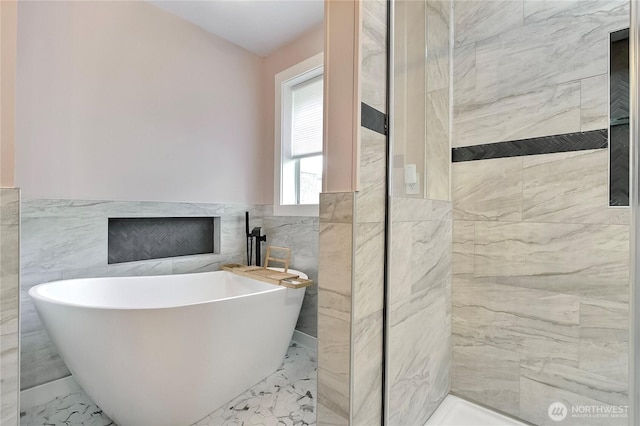 bathroom featuring tile walls, a soaking tub, marble finish floor, and a wainscoted wall
