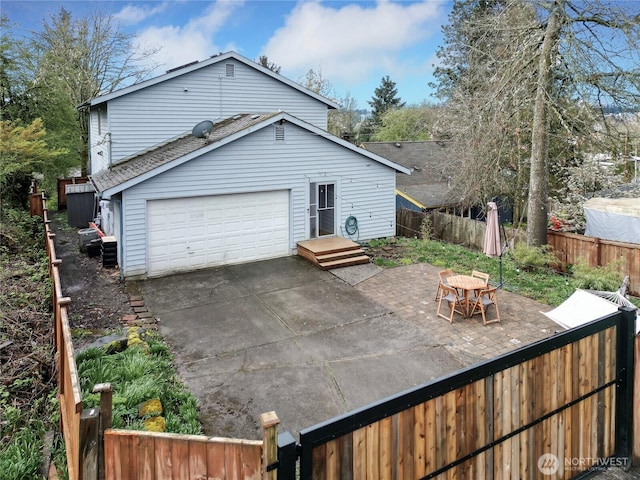 rear view of property featuring a garage, fence private yard, and driveway
