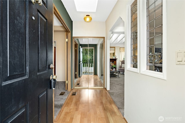 foyer entrance featuring a skylight, carpet flooring, visible vents, and wood finished floors