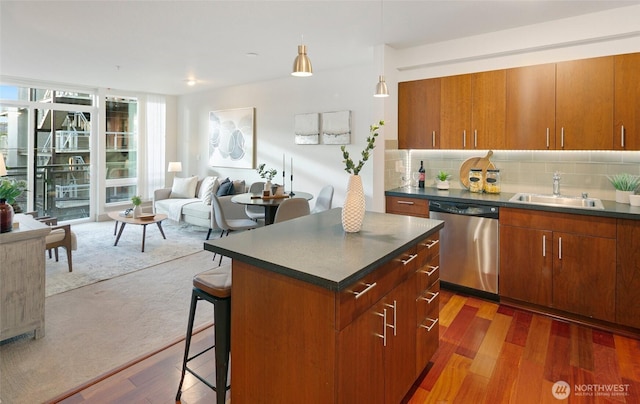 kitchen with dark countertops, decorative backsplash, stainless steel dishwasher, a sink, and a kitchen breakfast bar