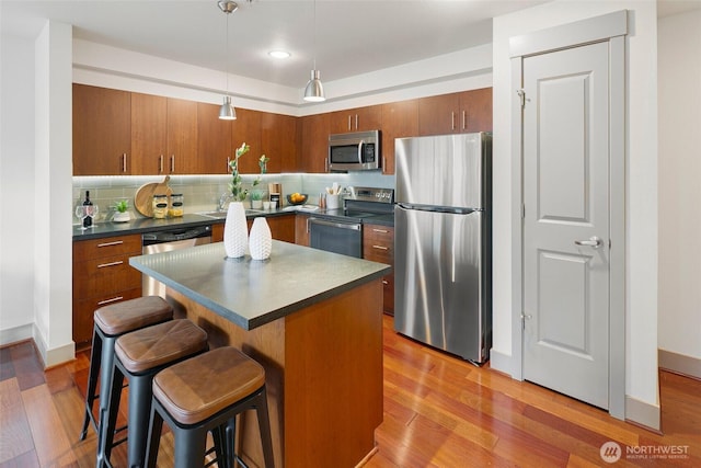 kitchen featuring stainless steel appliances, light wood-type flooring, dark countertops, and decorative backsplash