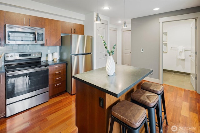 kitchen featuring dark countertops, a breakfast bar area, a center island, stainless steel appliances, and light wood-style floors