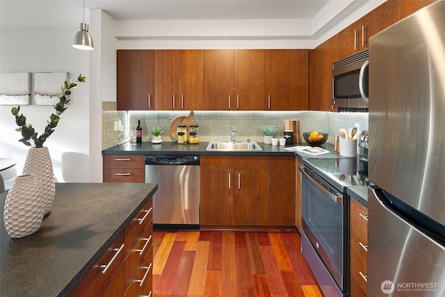 kitchen with stainless steel appliances, a sink, tasteful backsplash, dark countertops, and dark wood finished floors