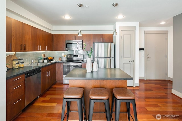 kitchen featuring stainless steel appliances, dark countertops, dark wood finished floors, and a breakfast bar