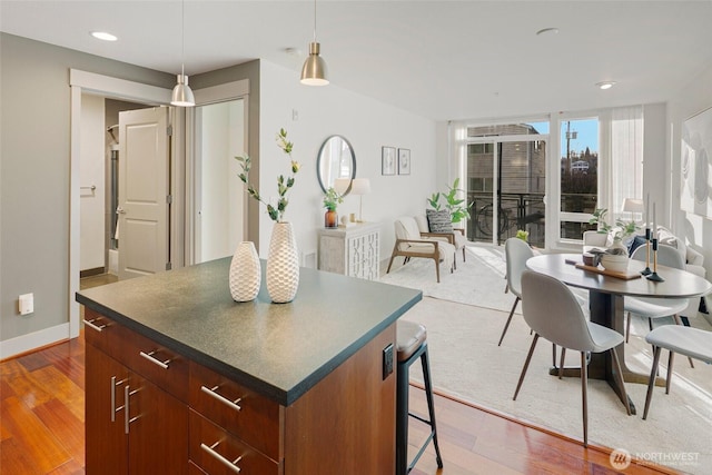 kitchen featuring a center island, decorative light fixtures, dark countertops, wood finished floors, and baseboards