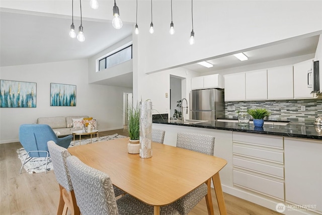 dining room with high vaulted ceiling, light wood finished floors, and baseboards