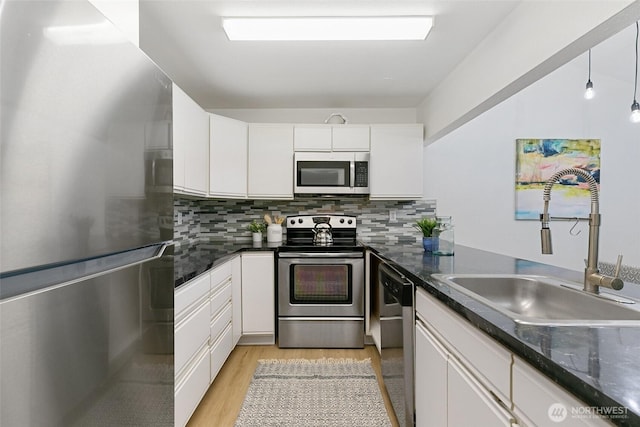 kitchen with decorative backsplash, appliances with stainless steel finishes, light wood-type flooring, white cabinetry, and a sink