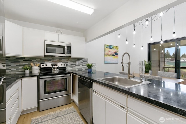 kitchen with decorative backsplash, appliances with stainless steel finishes, white cabinetry, a sink, and light wood-type flooring