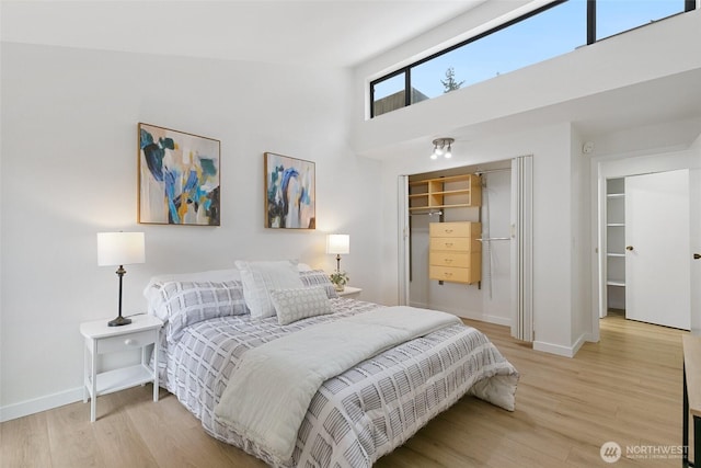 bedroom featuring a closet, a towering ceiling, light wood-style flooring, and baseboards