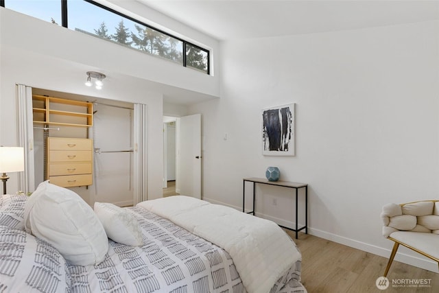 bedroom with a high ceiling, baseboards, and light wood finished floors