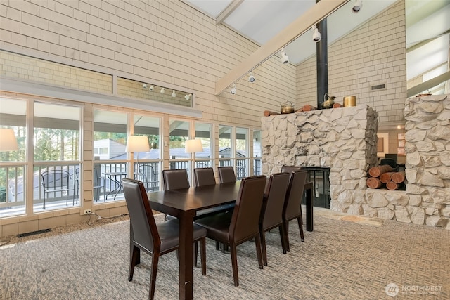 dining room with visible vents, a stone fireplace, carpet floors, high vaulted ceiling, and track lighting