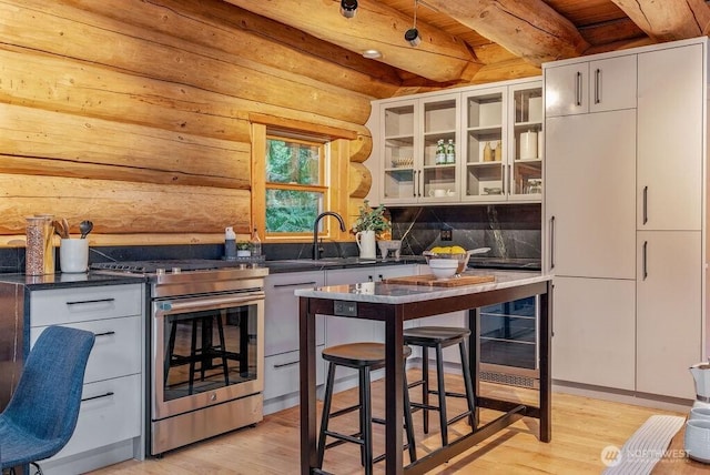 kitchen featuring stainless steel gas stove, dark countertops, glass insert cabinets, and light wood-style floors