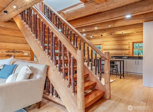 stairs with rustic walls, beamed ceiling, and wood finished floors