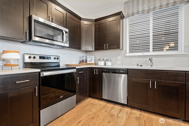 kitchen featuring sink, appliances with stainless steel finishes, dark brown cabinets, tasteful backsplash, and light wood-type flooring