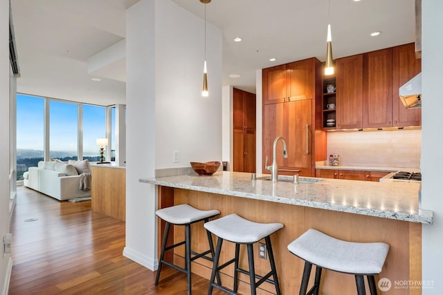 kitchen featuring sink, hanging light fixtures, exhaust hood, kitchen peninsula, and light stone countertops